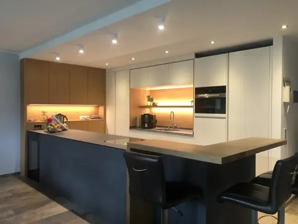 Moderne Einbauküche mit Kochinsel, Holz- und weißen Fronten sowie stimmungsvoller Beleuchtung.