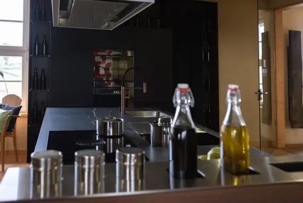 Moderne Designküche mit Kochinsel, Edelstahlarmatur und Gewürz- sowie Ölflaschen.