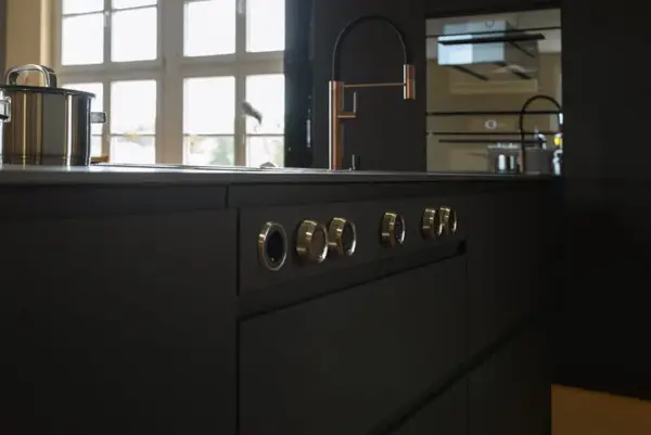 Moderne schwarze Küche mit Induktionskochfeld, Edelstahlarmatur und Topf am Fenster.