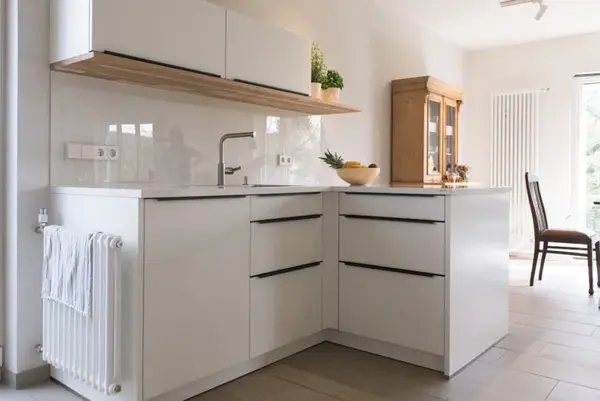 Moderne weiße Einbauküche mit Spüle, Hängeschränken und Essbereich am Fenster.