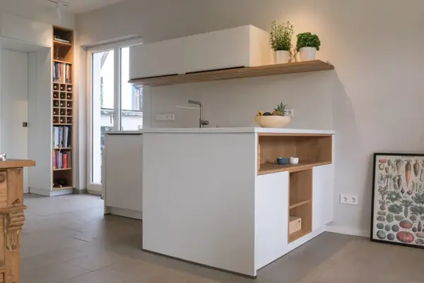 Moderne offene Küche mit weißen Schränken, Holzdetails und Pflanzen auf der Arbeitsplatte.