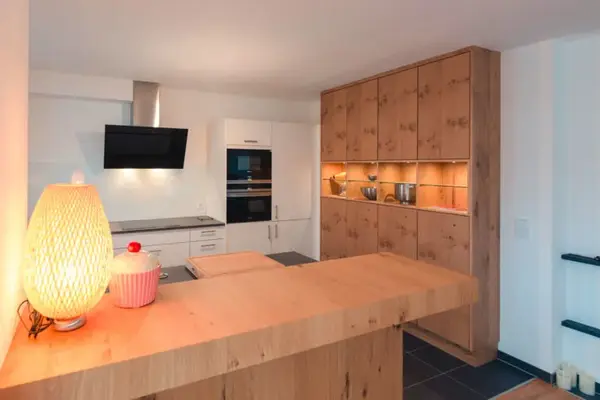 Moderne Einbauküche mit Holzfronten, Kücheninsel und beleuchteten Vitrinenschränken.