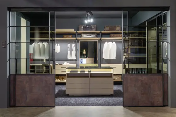 Moderner begehbarer Kleiderschrank mit Glasfront, Holzregalen und eleganter Beleuchtung.