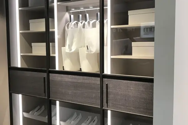 Moderner, beleuchteter Kleiderschrank mit Glastüren, Kleiderbügeln und Aufbewahrungsboxen.