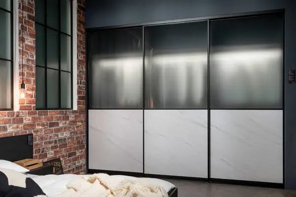 Moderner Kleiderschrank mit Schiebetüren aus Glas und Marmoroptik in einem Schlafzimmer.